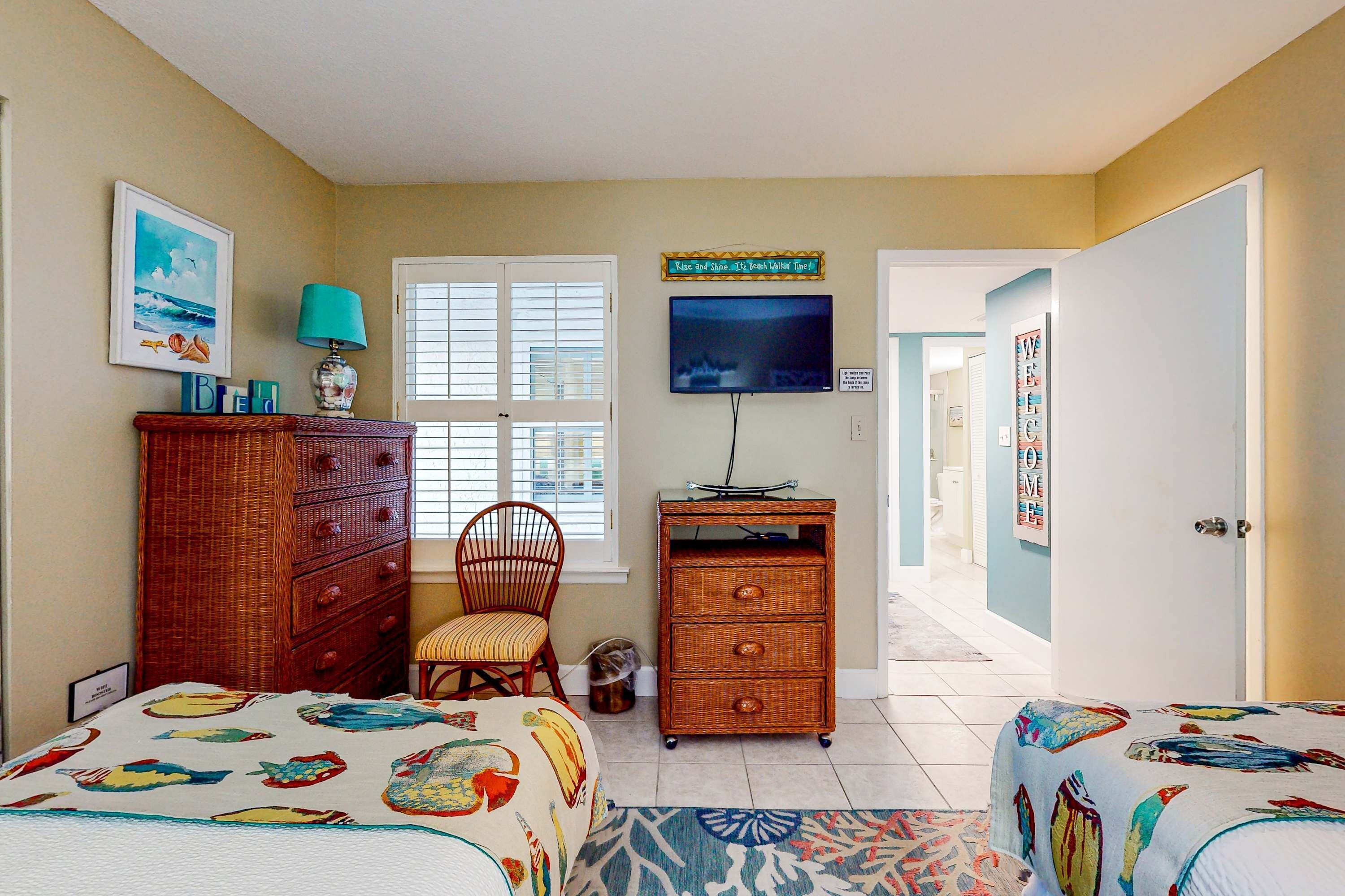 A bedroom with two beds, a dresser, a chair, a television, and a window with blinds.