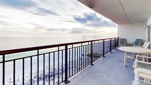 Un balcón con vista al mar, una mesa con sillas y una barandilla.