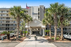 A hotel entrance with a flag, palm trees, and a parking area. - 6th-floor, bright Gulf-front condo with views - close to entertainment (Fort Walton Beach)