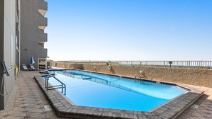 Una piscina con solárium de losetas de piedra, un puesto de socorrista y vista al mar.