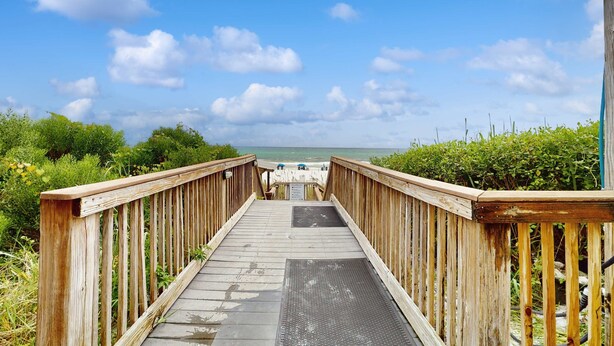 Une promenade en bois menant à une plage, avec un ciel dégagé.