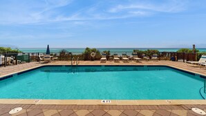 Une piscine rectangulaire à l’eau d’un bleu limpide, entourée de chaises longues et d’une clôture, et offrant une vue sur une étendue d’eau.
