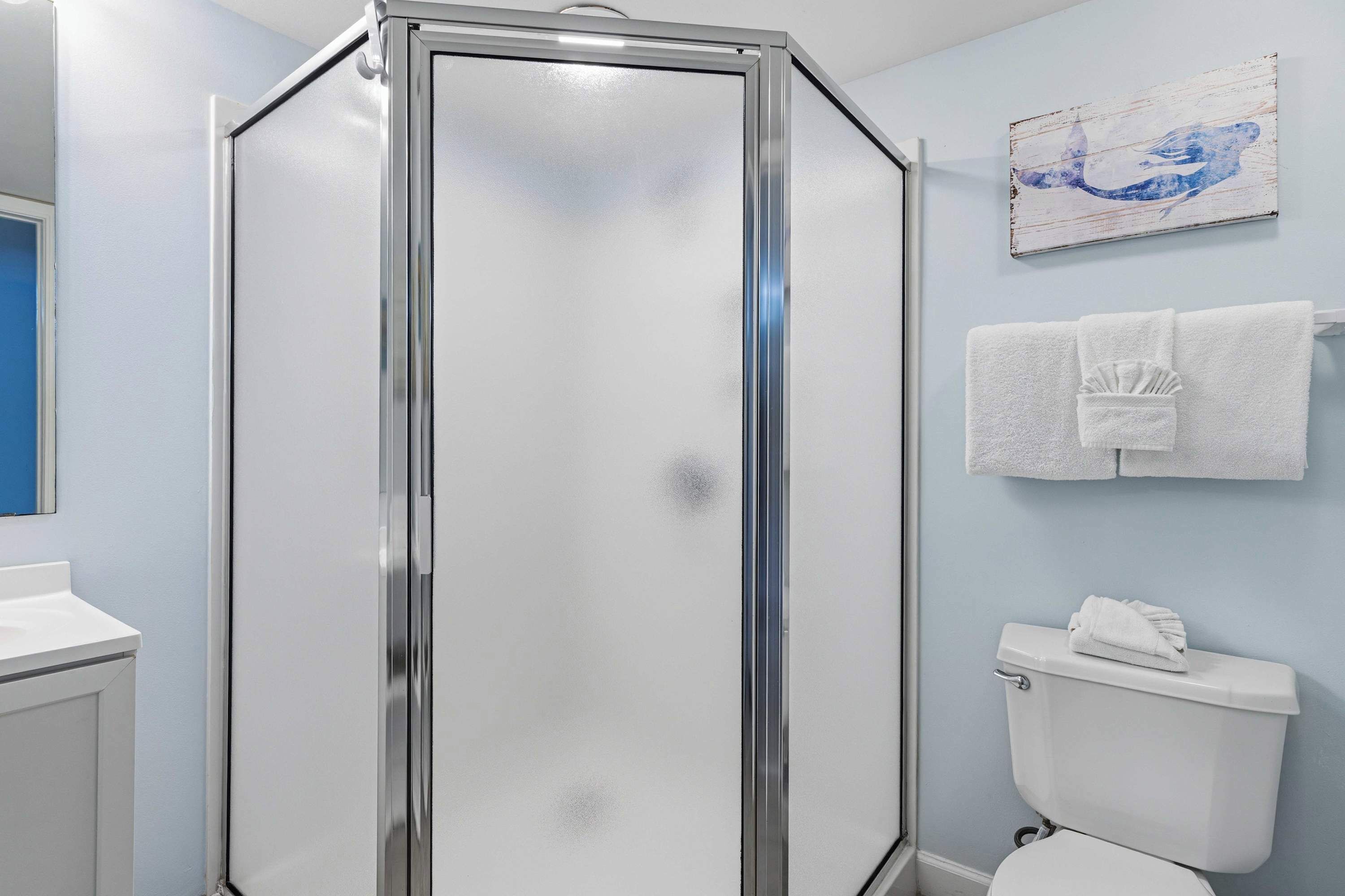 A bathroom with a glass-enclosed shower, a white toilet, and a towel rack with towels.