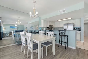 A modern kitchen with white cabinets, a central island, and a dining area with white chairs. - Oceanfront condo with washer&dryer, pool access, ocean view, and central AC (Fort Walton Beach)