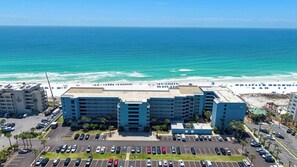 A multi-story hotel with a parking lot in front, a beach with umbrellas, and a view of the ocean. - Oceanfront condo with washer&dryer, pool access, ocean view, and central AC (Fort Walton Beach)