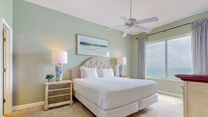 Una camera da letto con un letto, comodini, una ventola a soffitto, una finestra con tende e un quadro appeso al muro.