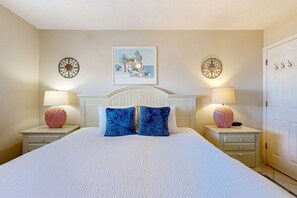 Un dormitorio con una cama grande, dos mesitas de noche con lámparas, una decoración de pared y una puerta con pomo.