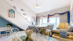 A living room with a glass dining table, white chairs, a grey sofa, and a TV. - Gulf-front condo with complimentary beach equipment - near shops & dining (Destin)