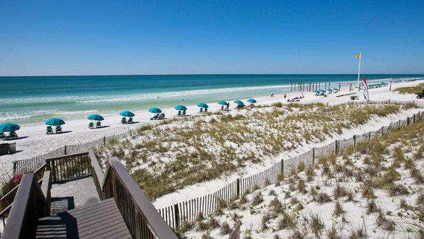 A beach with a wooden boardwalk, beach umbrellas, and a flag. - Gulf-front condo with complimentary beach equipment - near shops & dining (Destin)