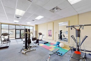 Une salle de sport équipée de machines de cardio, d’appareils de musculation, d’un tapis coloré et d’un miroir.