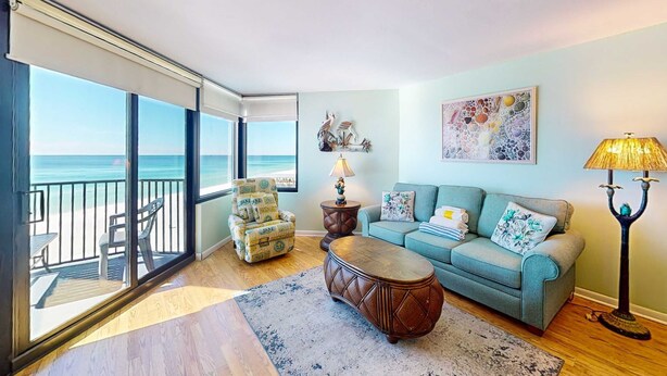 A living room with a view of the ocean, a sofa, a coffee table, and a lamp. - Gulf-view condo with furnished balcony, pools, beach access, fitness room (Panama City Beach)