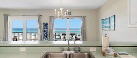 A kitchen with a double sink, a chandelier, and a view of the beach.