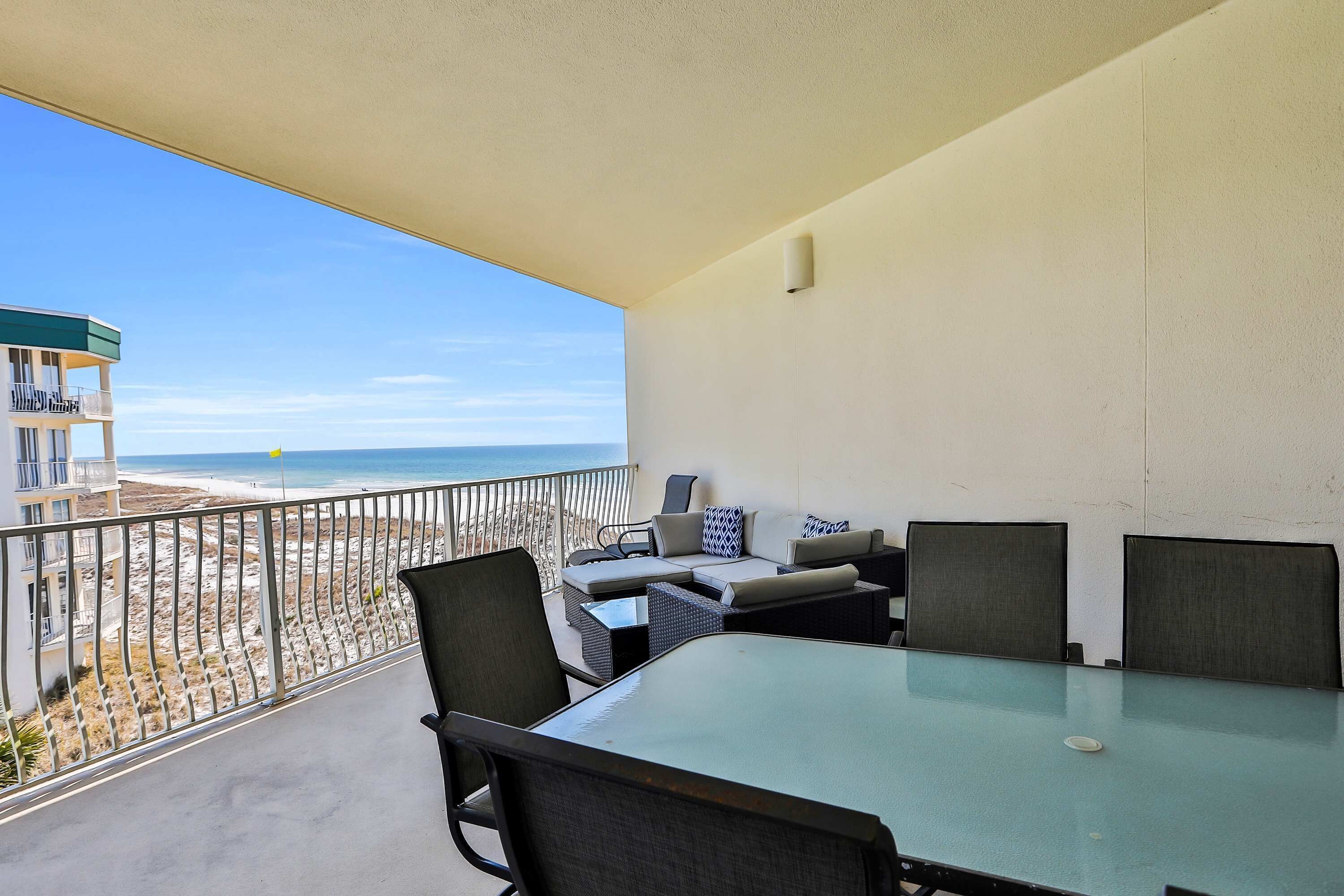 A balcony with a glass table and chairs, a sofa, and a view of the beach and ocean.