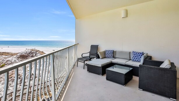 Ein Balkon mit Blick auf den Strand, ausgestattet mit einer Couch, Stühlen und einem Couchtisch.