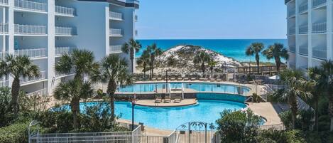 A resort with a central pool, multiple balconies, and a view of the ocean.