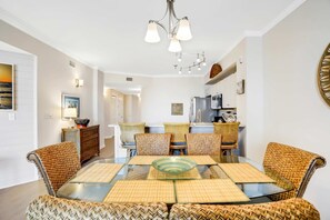 A dining area with a glass table, woven chairs, and a chandelier. - Oceanfront condo with pool, hot tub, sauna, gym, bikes, tennis - lovely balcony (Santa Rosa Beach)