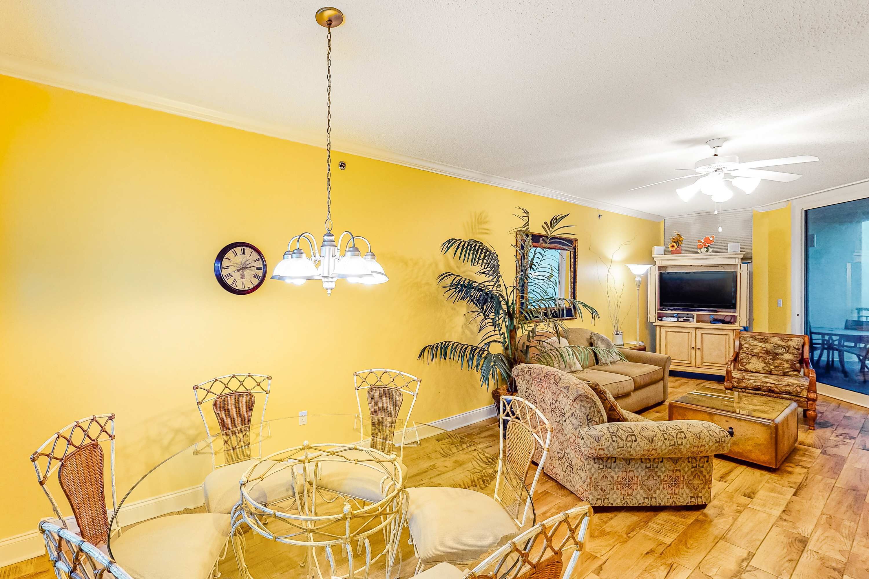 A living room with yellow walls, a chandelier, a sofa, a coffee table, and a television.