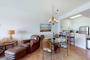 A living room with a glass dining table, leather sofa, and a kitchen in the background.