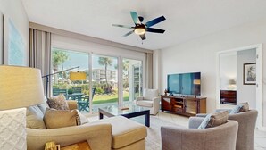 A modern living room with a sofa, armchairs, a coffee table, a TV, and a ceiling fan. - Coastal condo with lagoon pool, bike rentals, tennis, pickleball & beach access (Seacrest)