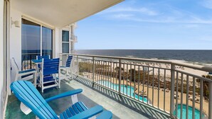 Een balkon met blauwe stoelen en een zwembad, met uitzicht op een strand en de oceaan.