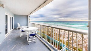 Ein Balkon mit weißem Tisch und Stühlen, der auf einen Strand mit Geländer blickt.