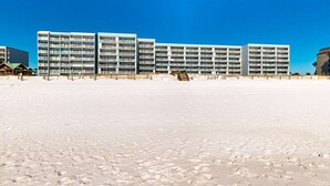Ein Strandhotel mit mehreren Etagen, Balkonen und einem Sandstrand im Vordergrund.