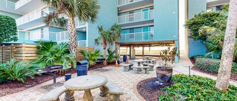A courtyard with outdoor seating, palm trees, and a building with balconies.