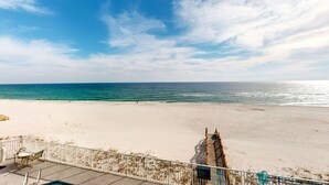 En strand med en træterrasse og stole, et skilt der angiver et strandområde, og et klart havudsigt.