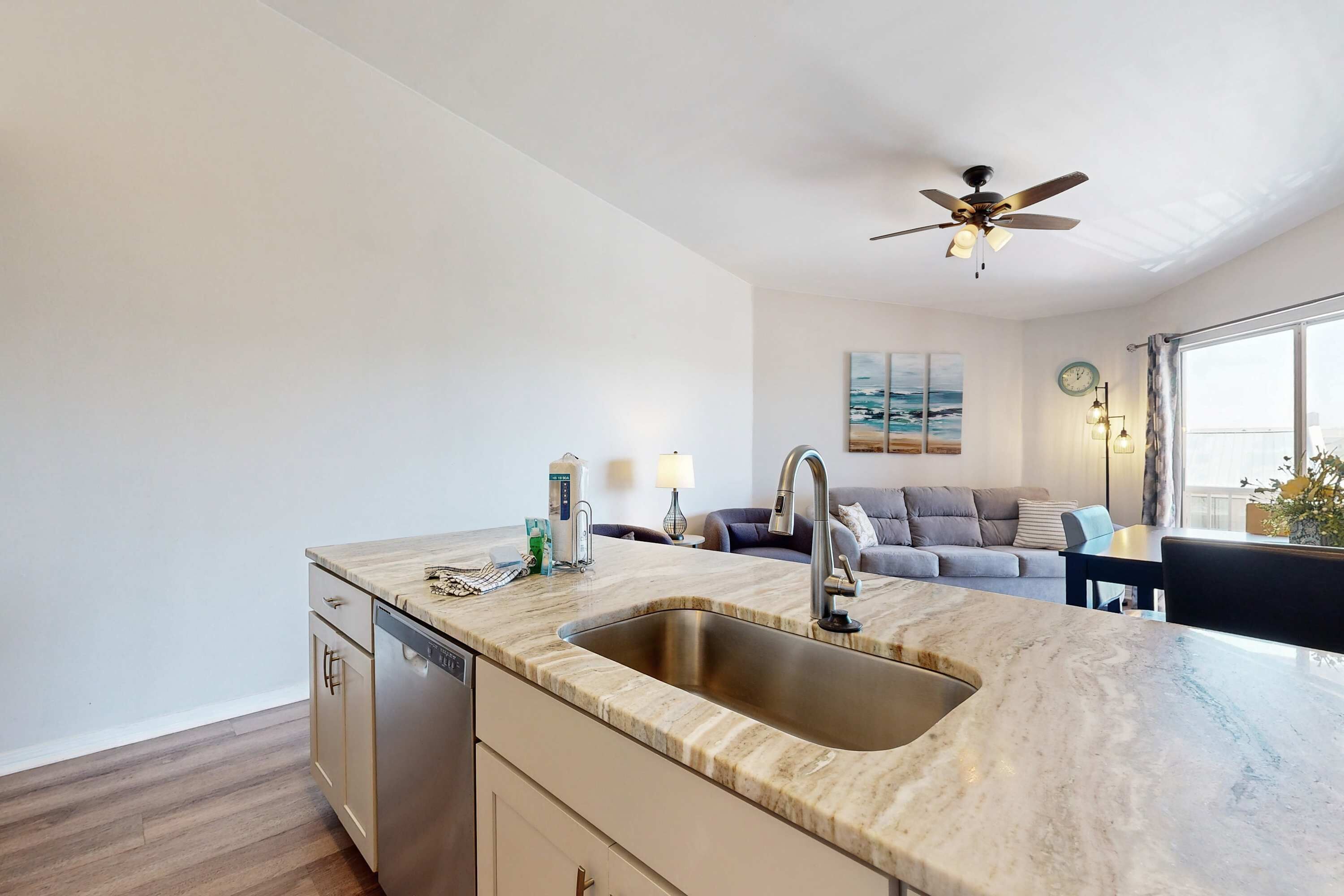 A modern kitchen with a built-in dishwasher, a marble countertop, and a ceiling fan.