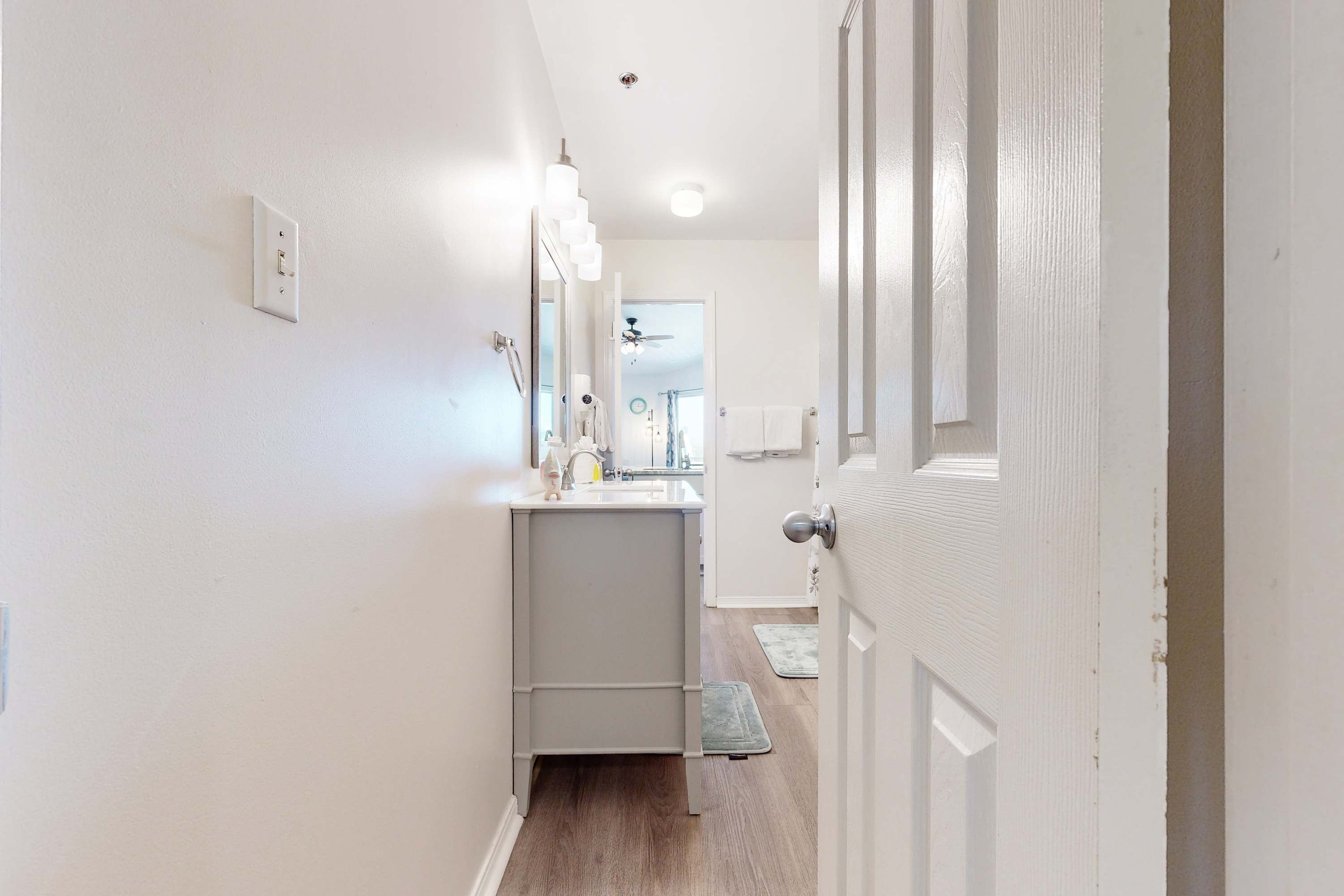 A narrow hallway with a bathroom featuring a sink, mirror, and towel rack.