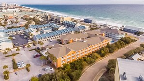 An aerial view of a coastal hotel with multiple buildings, a parking lot, and a beach in the background. - Condo with Pool Amenity in Miramar Beach (Miramar Beach)