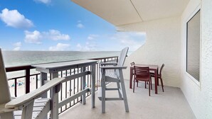 A balcony with a view of the beach and ocean, a table with chairs, and a large window. - Cozy beachfront condo with beach setup - near shopping (Fort Walton Beach)