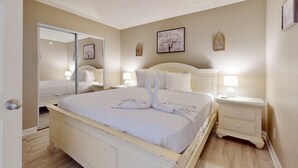 A bedroom with a bed, bedside tables, a mirror, and wall decorations. - Cozy beachfront condo with beach setup - near shopping (Fort Walton Beach)