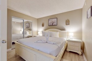 A bedroom with a bed, bedside tables, a mirror, and wall decorations. - Cozy beachfront condo with beach setup - near shopping (Fort Walton Beach)