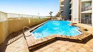 A swimming pool with a tiled deck, a metal ladder, and a white railing. - Cozy beachfront condo with beach setup - near shopping (Fort Walton Beach)