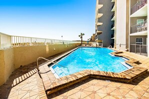 A swimming pool with a tiled deck, a metal ladder, and a white railing. - Cozy beachfront condo with beach setup - near shopping (Fort Walton Beach)