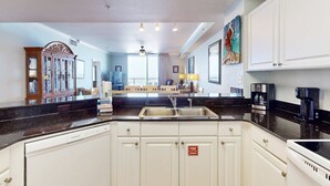 A kitchen with white cabinets, a black countertop, a stainless steel sink, and a ceiling fan. - Waterfront Panama City Beach escape with pools, hot tubs & fitness room (Panama City Beach)