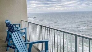 A balcony with two blue Adirondack chairs, a railing, and a view of the ocean with a pier in the distance. - 21st-floor oceanfront condo with ocean view, pool & hot tub access & W/D (Panama City Beach)