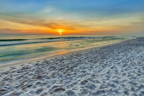 A beach with footprints leading to the water, a sunset in the background, and a clear sky. - Spacious condo with full kitchen, shared pool and beachfront (Panama City Beach)