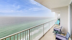 A balcony with a view of the ocean, a railing, and a seating area with chairs and a table. - Gulf-front, 25th-floor condo with WiFi & on-site pools, hot tubs, gym, game room (Panama City Beach)