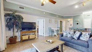 A living room with a television, sofa, coffee table, and a ceiling fan. - Gulf-front, 25th-floor condo with WiFi & on-site pools, hot tubs, gym, game room (Panama City Beach)