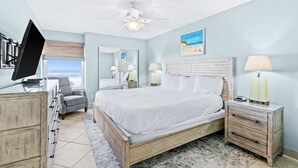 A bedroom with a bed, a desk, a chair, a nightstand, a lamp, a ceiling fan, and a window with a view. - Comfortable beachfront condo with beach service - quick drive to dining (Fort Walton Beach)