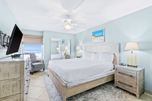A bedroom with a bed, a desk, a chair, a nightstand, a lamp, a ceiling fan, and a window with a view. - Comfortable beachfront condo with beach service - quick drive to dining (Fort Walton Beach)