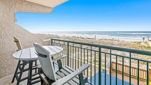 A balcony with a table and chairs overlooking a beach. - Comfortable beachfront condo with beach service - quick drive to dining (Fort Walton Beach)