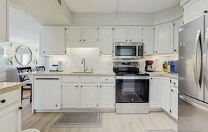 A modern kitchen with white cabinets, stainless steel appliances, a microwave, oven, and a refrigerator. - Updated beachfront condo with beach setup & quick drive to entertainment (Fort Walton Beach)