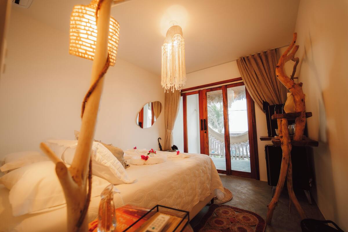 Een hotelkamer met een bed, een hanglamp, een spiegel en een houten sculptuur.