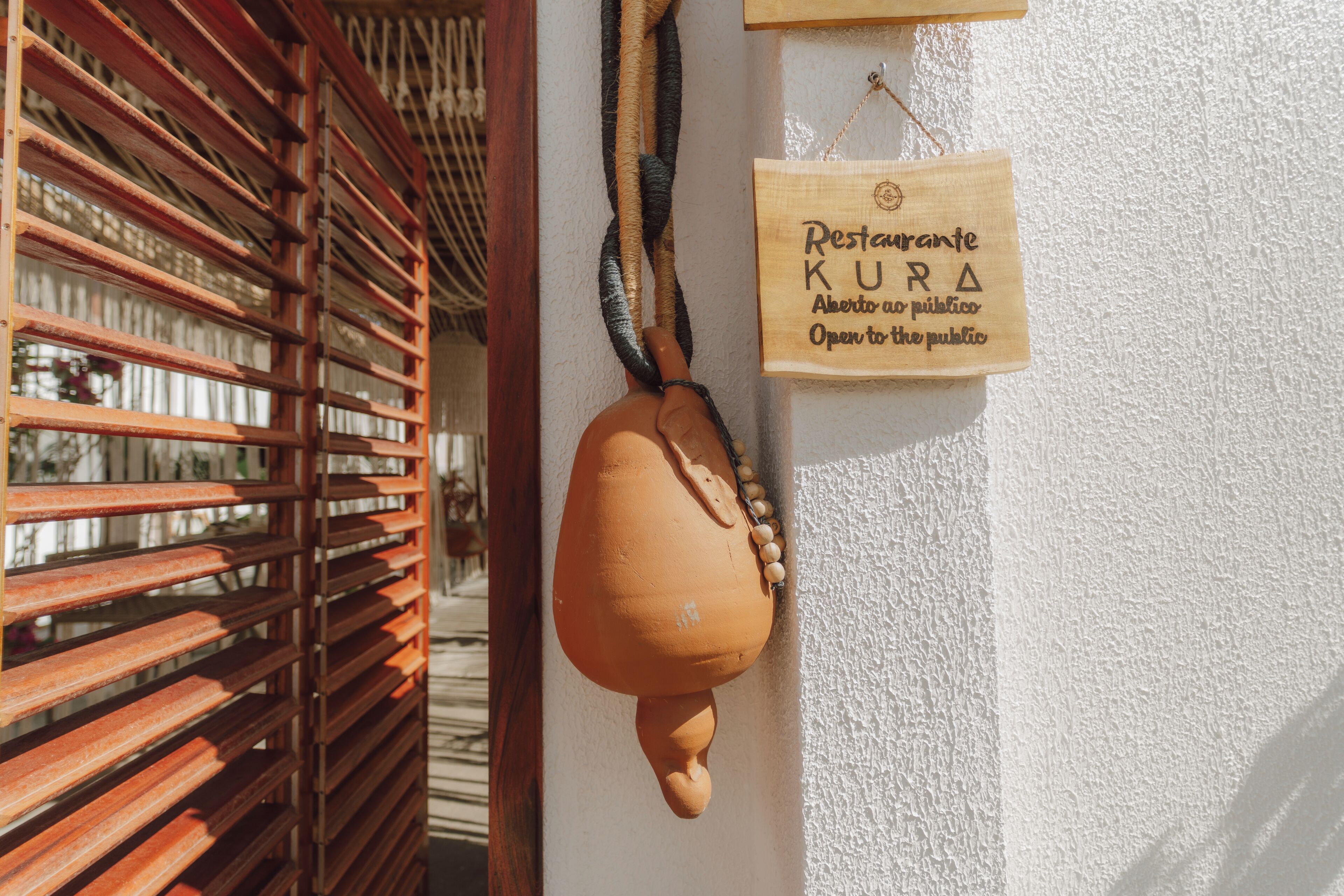 A rustic wall with a wooden slatted door and a hanging clay pot. A wooden sign with text is attached to the wall.