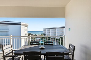 Un balcón con mesa y sillas, con vista a una piscina y una playa.