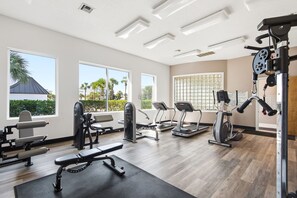 Ein Fitnessstudio mit verschiedenen Trainingsgeräten, großen Fenstern und Blick auf Palmen.