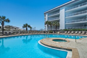A swimming pool with a hot tub, surrounded by lounge chairs and palm trees, with a building in the background. - Magical 3rd-floor condo with pools, telescope for stargazing & pickleball (Santa Rosa Beach)